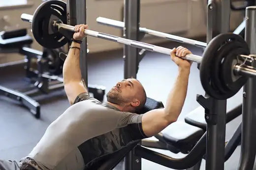 Man lifting weights on bench press in gym with adjustable barbell.