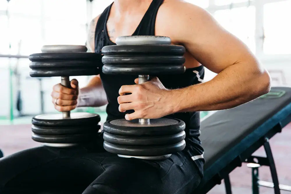 Person holding adjustable dumbbells in a gym setting, showcasing versatile gym equipment for home fitness and strength training.