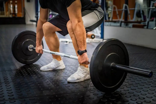 Person performing a deadlift with a barbell in a gym, focusing on lower body strength and core stability with gym equipment.