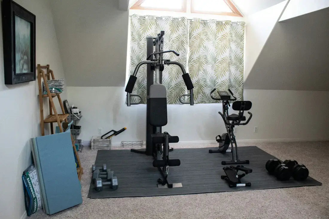 Affordable home gym setup with dumbbells, adjustable bench, and exercise bike in a cozy attic space.