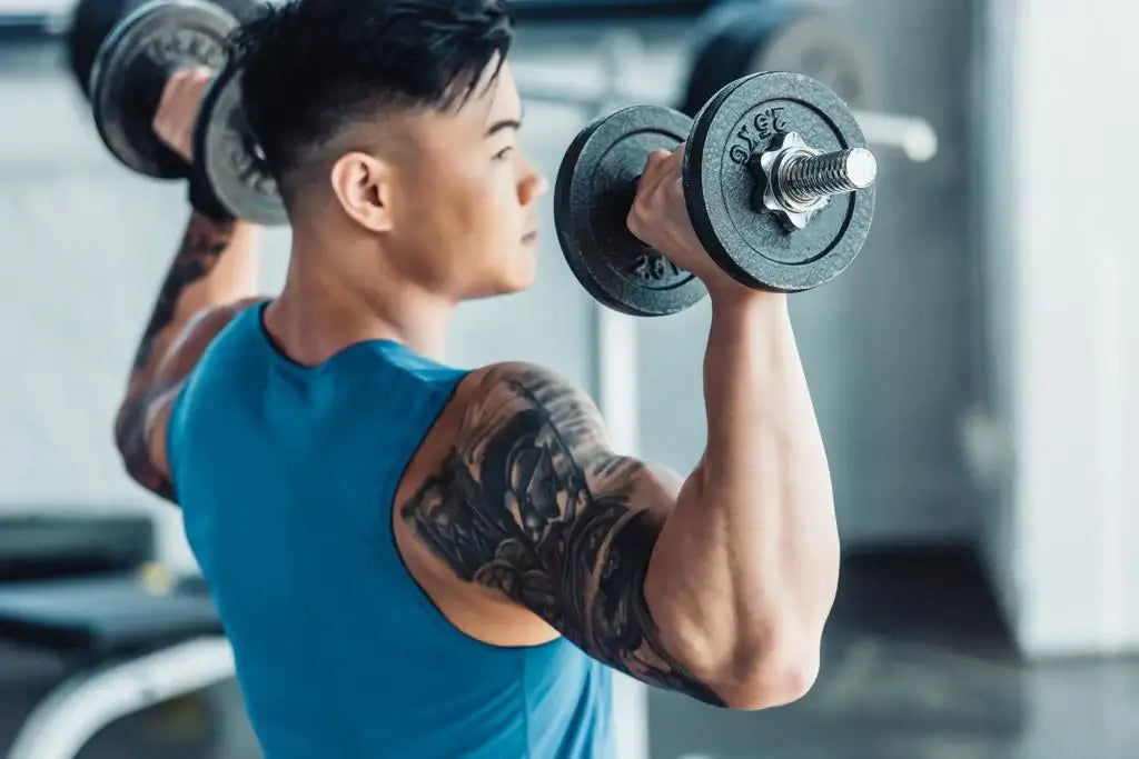 Person performing shoulder press exercise with dumbbells in gym setting.