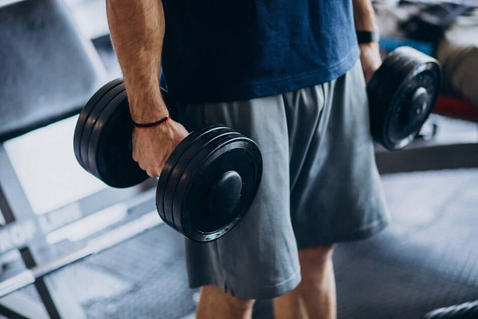 Person holding adjustable dumbbells in a home gym setup, showcasing gym equipment options for cost-effective workouts at home.