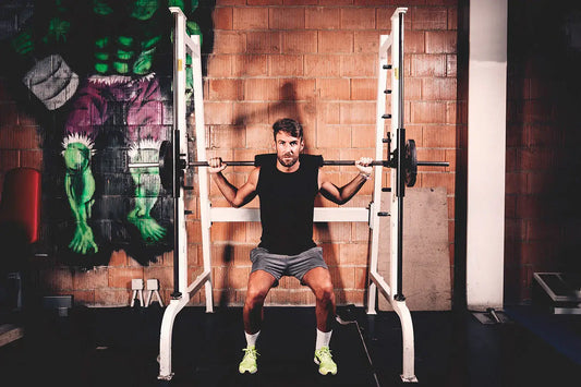 Man performing squats with a barbell in a gym setting featuring gym equipment and motivational wall art.