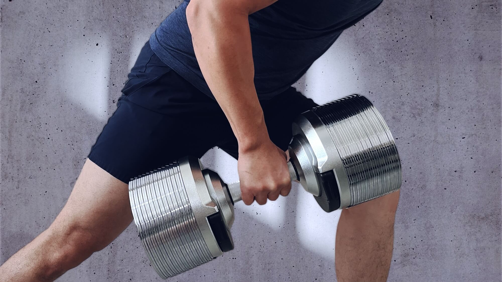 Person lifting adjustable dumbbell in gym; gym equipment workout with kettlebell and weights.